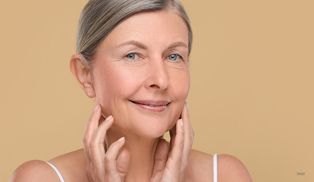 a woman frames her flawless face with her hands against a goldenrod background